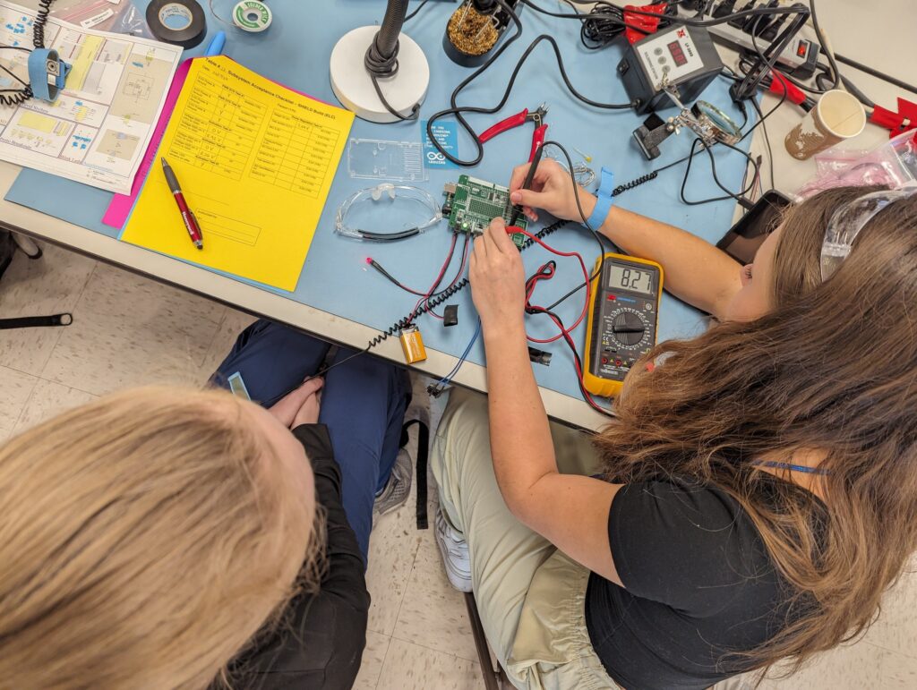 Students sitting at table using electronic test equipment on circuit board