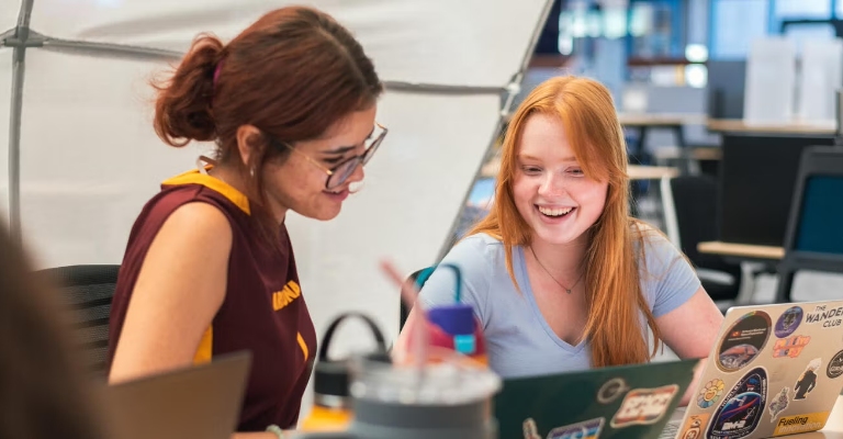Two young women work on laptop computers
