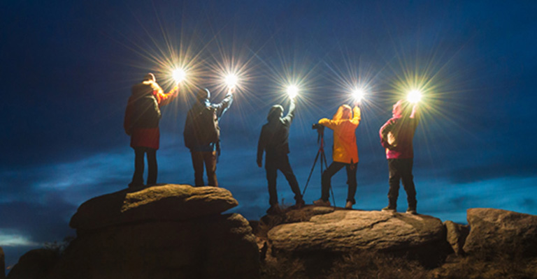 Five people shining lights at night sky