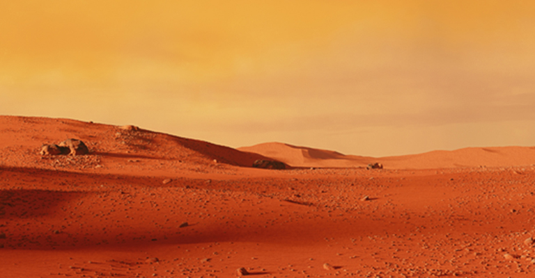 The Martian landscape of red-orange dust, rocks and hills against a lighter orange sky