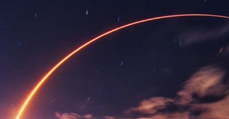 A launching spacecraft makes a glowing arc in the evening sky